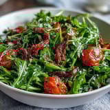 Fresh dandelion greens salad with lemon vinaigrette and Parmesan shavings, topped with cherry tomatoes and toasted pine nuts for a vibrant, tangy bite.