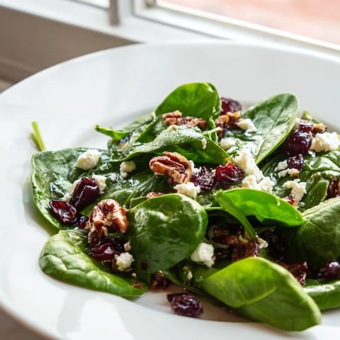 Fresh baby spinach and candied pecans in a spinach goat cheese salad, tossed with balsamic vinaigrette on a rustic wooden table.