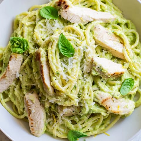 A bowl of creamy avocado chicken pasta tossed with ripe avocado sauce and topped with grated Parmesan cheese.