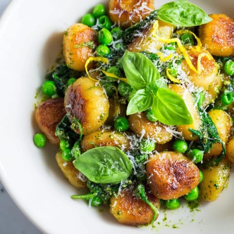 A close-up of Pesto Pea Gnocchi Skillet, finished with grated Parmesan and fresh basil leaves.  